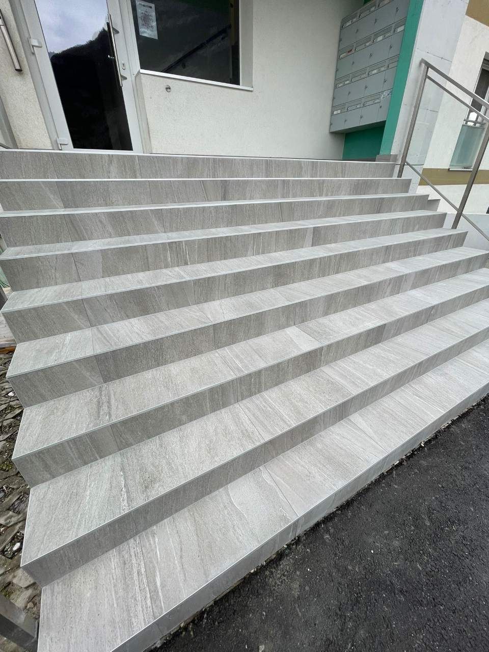 Escalier extérieur carrelé de gris menant à l'entrée d'un bâtiment.