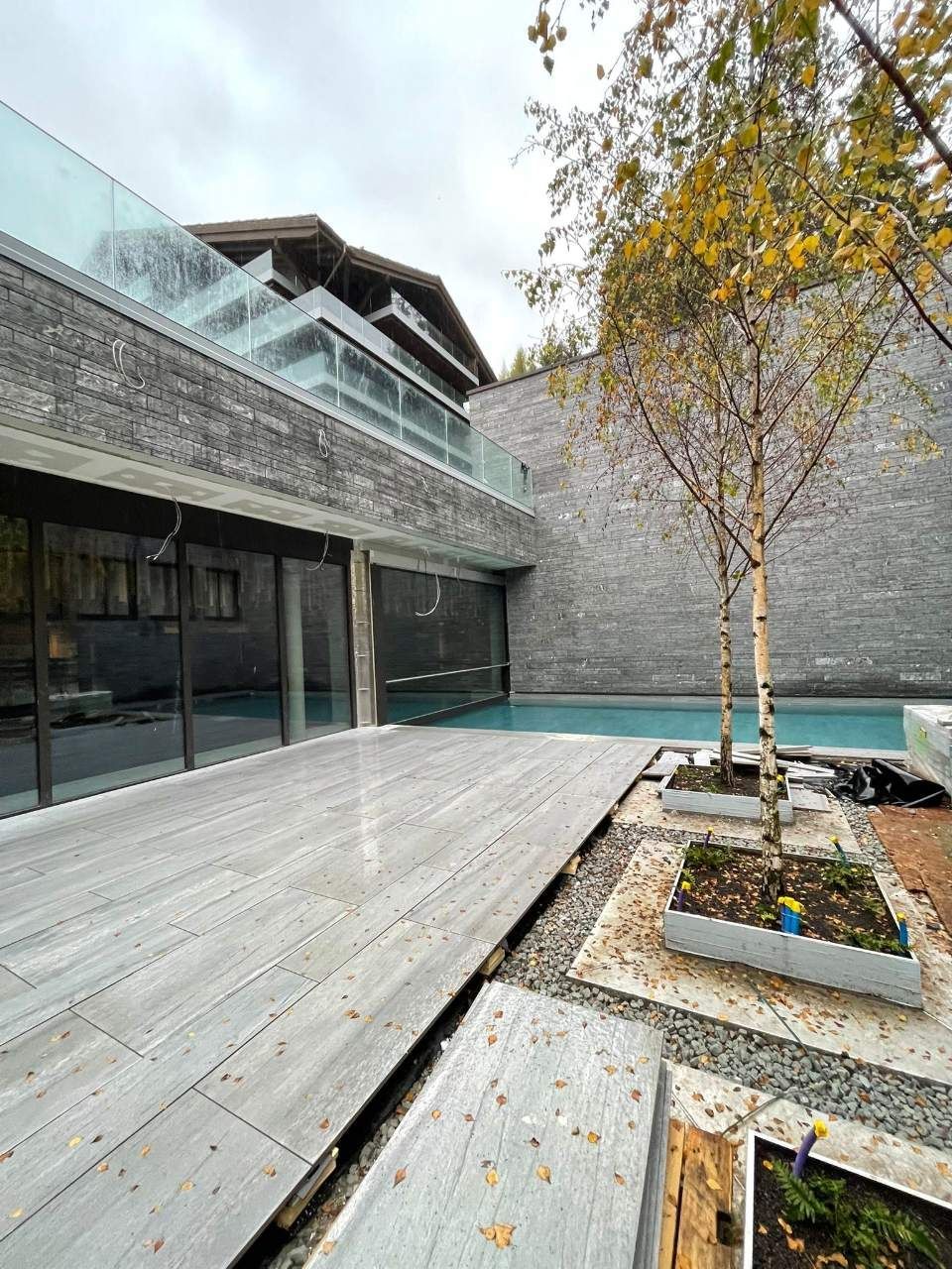 Maison moderne avec façade en pierre grise, piscine et terrasse en bois.