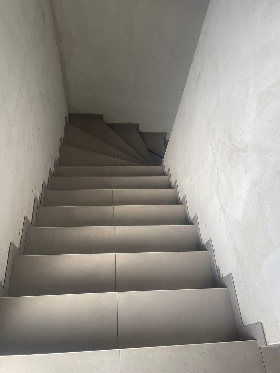 Escalier aux marches carrelées de gris menant vers le haut entre des murs blancs.