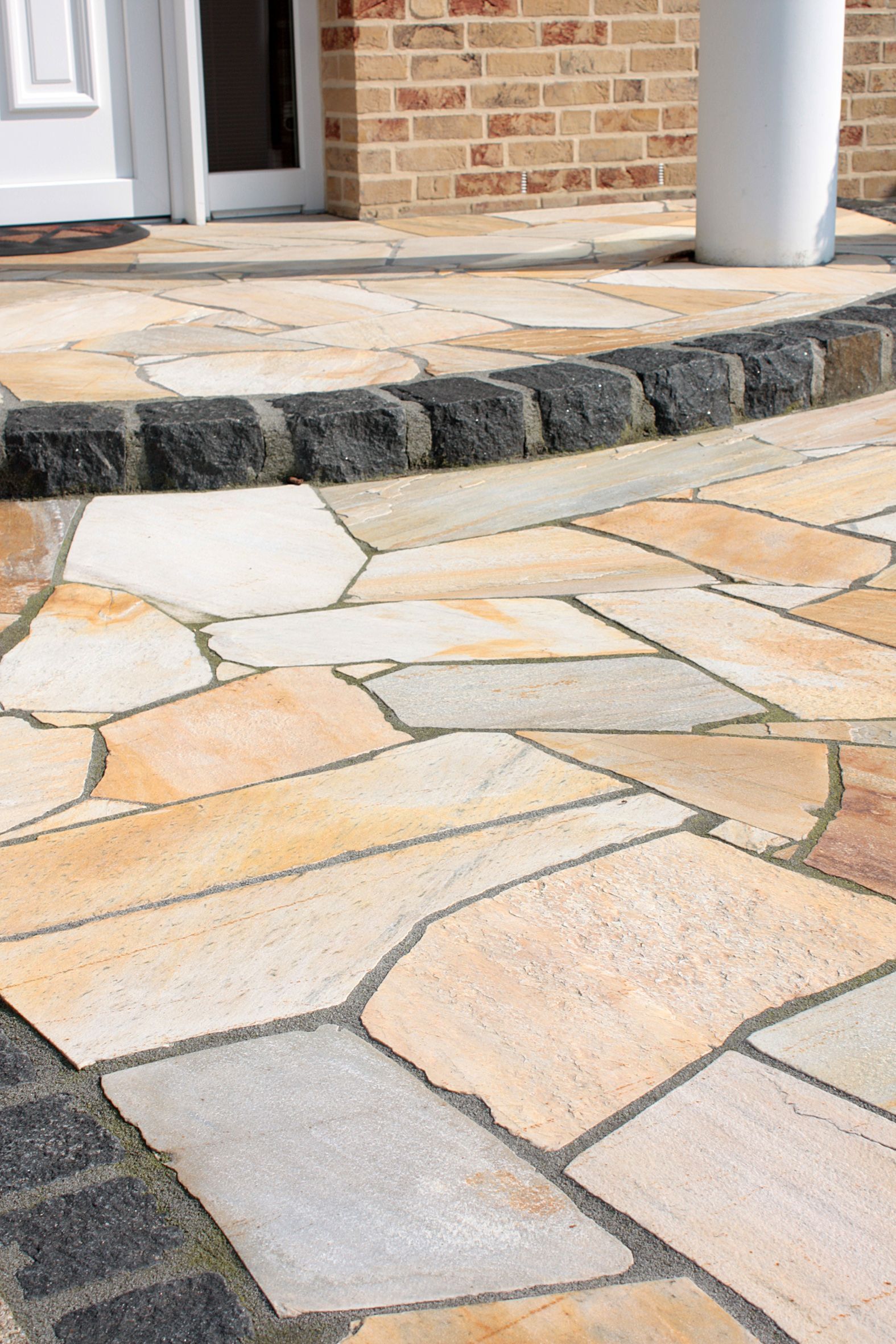 Detailansicht einer Naturstein-Terrasse mit harmonisch abgerundeter Stufe und dunkler Pflasterstein-Einfassung