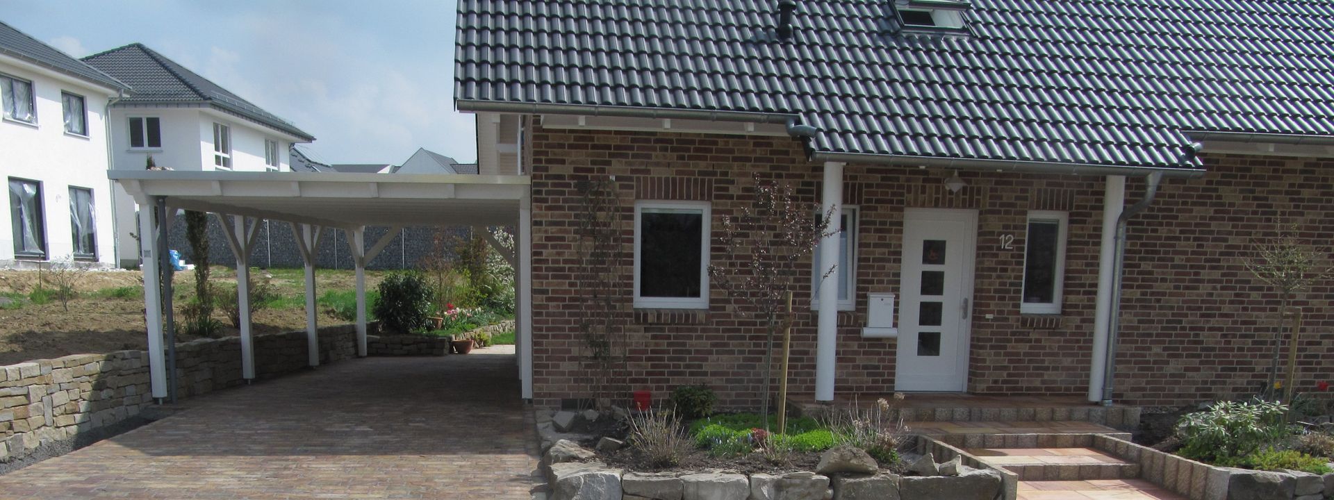 Ansicht eines Einfamilienhauses mit Klinkerfassade, weißer Haustür und angrenzendem Carport.