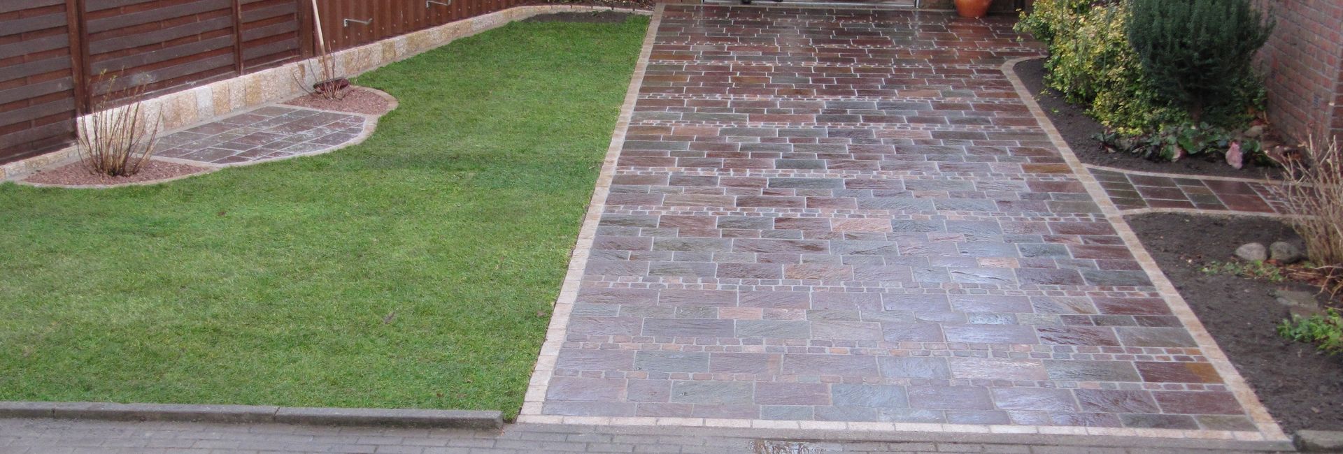 Klarer Übergang zwischen einer frischen Rasenfläche und einem rot-braunen Pflastersteinweg im Garten.