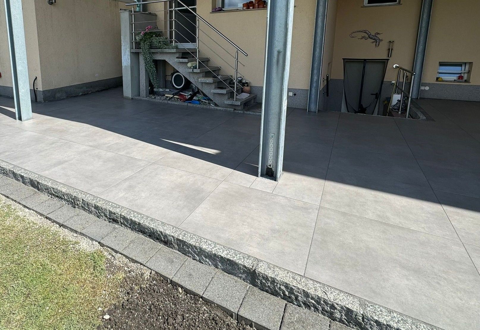 Moderne, großformatige graue Terrassenplatten im Außenbereich mit Überdachung und Metallstützen