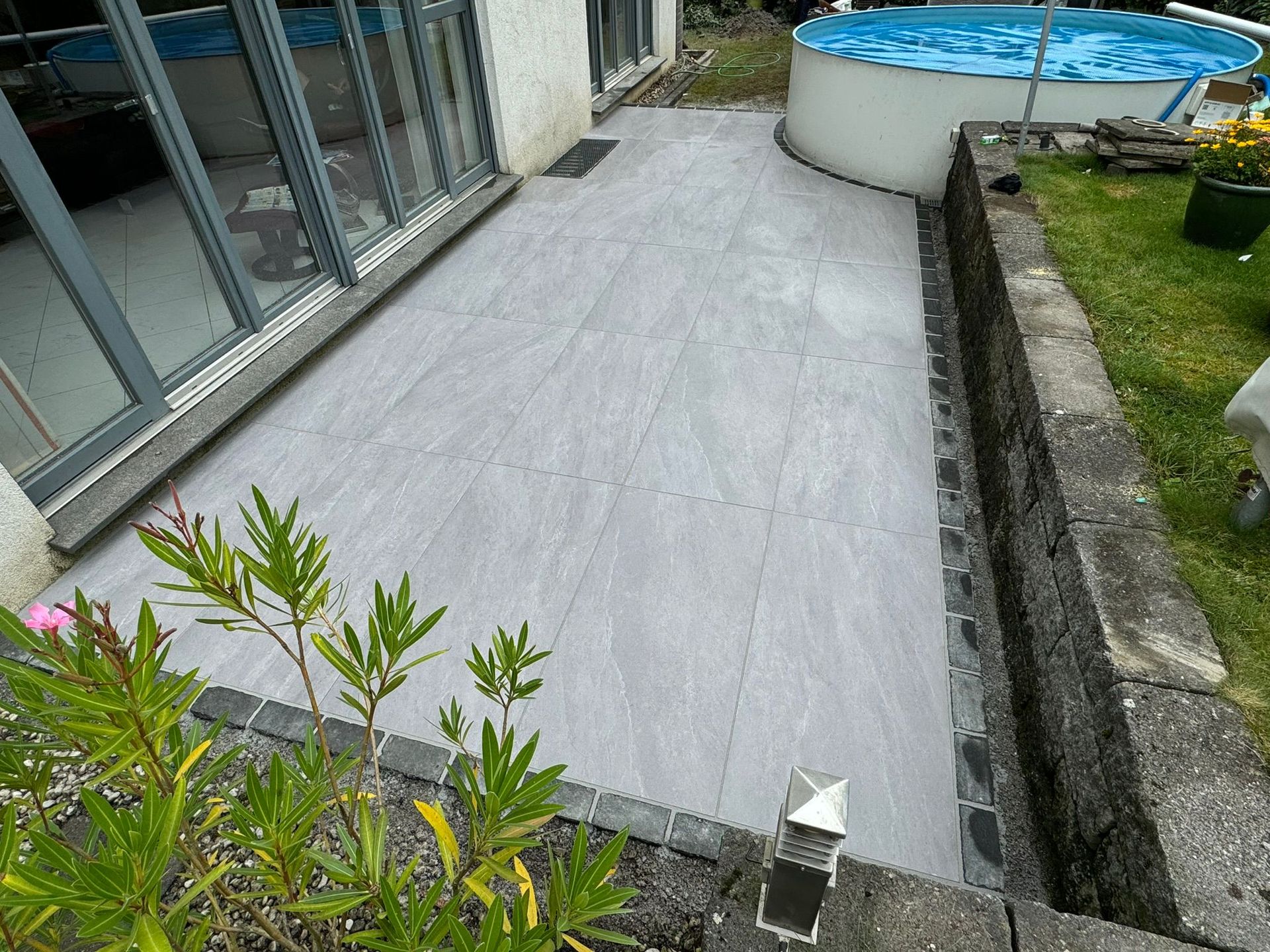 Moderne graue Terrassenplatten verlegt im Außenbereich neben einem Aufstellpool und Rasen