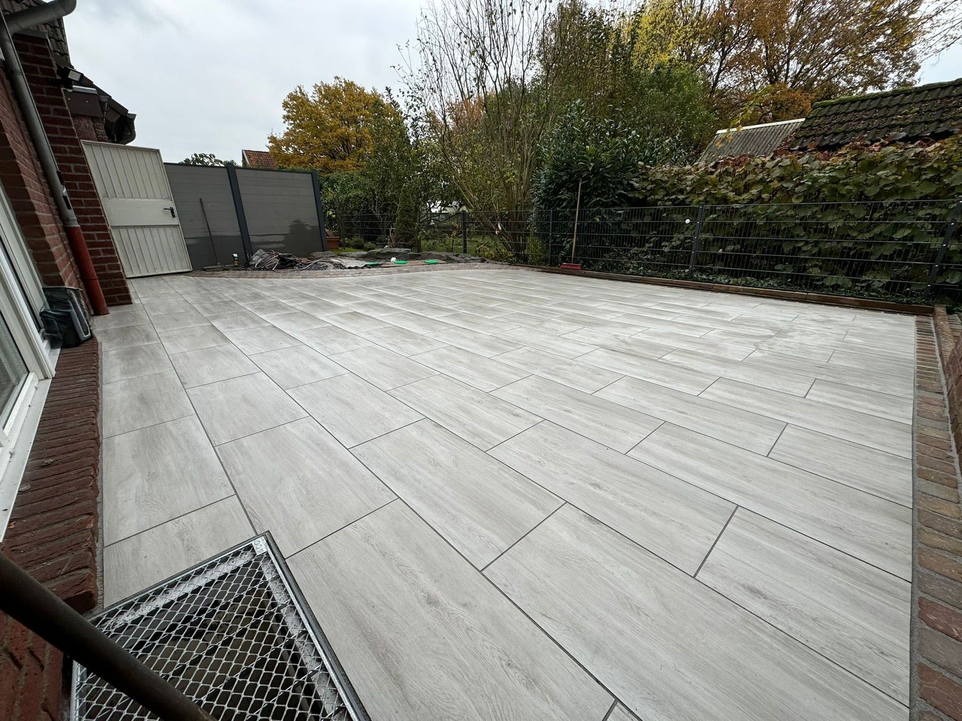 Moderne, großformatige helle Terrassenplatten, verlegt in einem Außenbereich mit angrenzendem Rasen