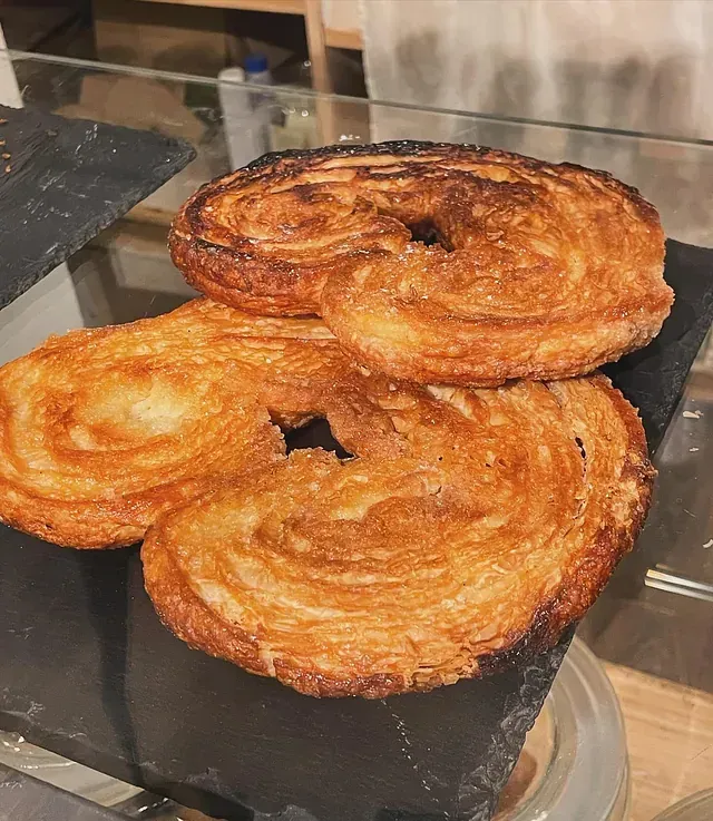 Tres palmeras de color marrón dorado, o pasteles con forma de oreja de elefante, sobre una superficie de pizarra negra.
