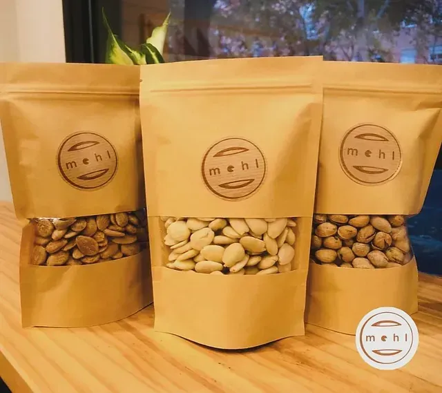 Tres bolsas de papel marrón con una ventana transparente que muestra semillas pálidas; cada bolsa tiene un logotipo 