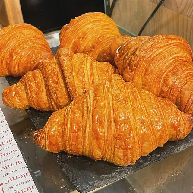 Croissants dorados y hojaldrados dispuestos sobre una superficie oscura, probablemente en una panadería.