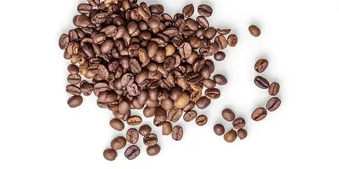 Un montón de granos de café tostados esparcidos sobre una superficie blanca. Los granos presentan diversos tonos de marrón.