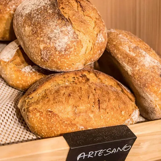 Varias hogazas de pan artesanal en un estante de madera con un cartel de 