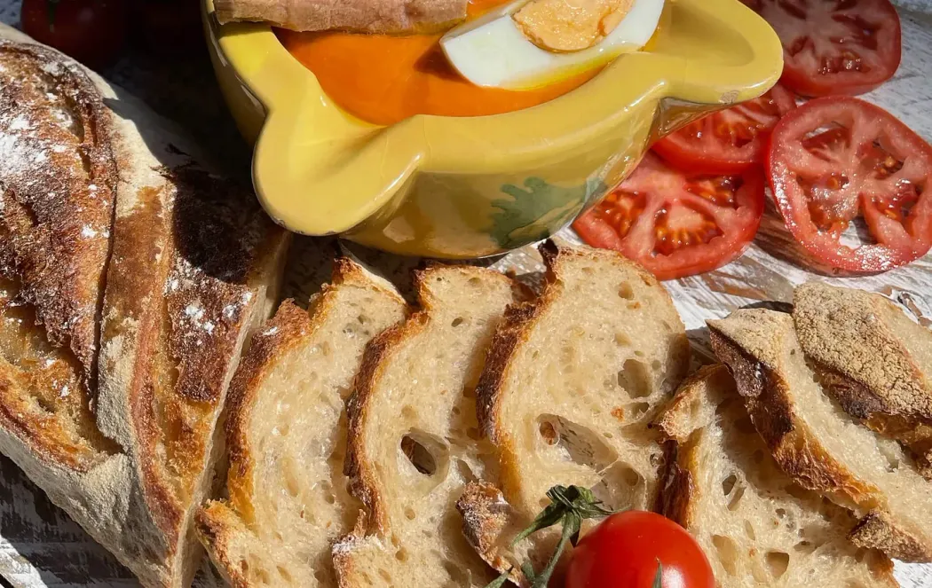 Pan de molde, tomates y un plato amarillo con salsa de naranja, posiblemente salmorejo, cubierto con huevo y atún.