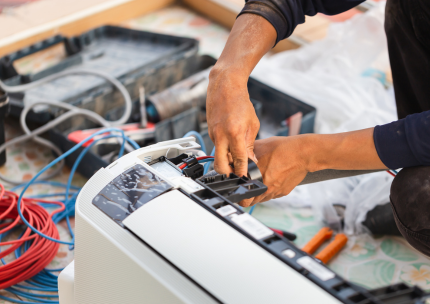 Un homme répare un climatiseur avec une paire de pinces.