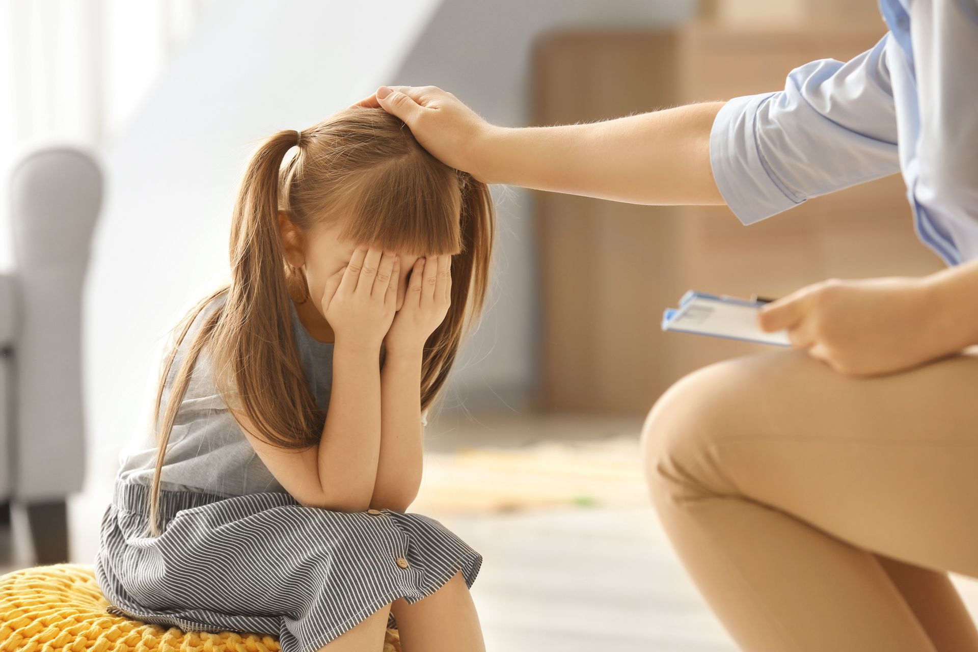 Un niño con la cara entre las manos es reconfortado por la mano de un adulto sobre su cabeza, en una habitación.