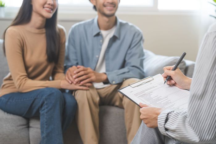 Pareja tomada de la mano, sonriendo durante una sesión de terapia con un terapeuta tomando notas en una habitación luminosa.
