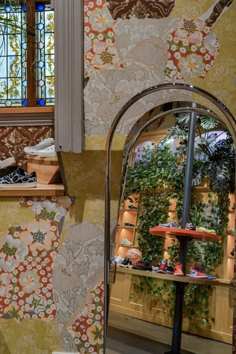 Ein Spiegel in einem Raum mit einem Buntglasfenster und einem Regal mit Schuhen darauf.