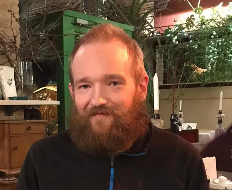 Ein Mann mit Bart steht vor einer grünen Tür.