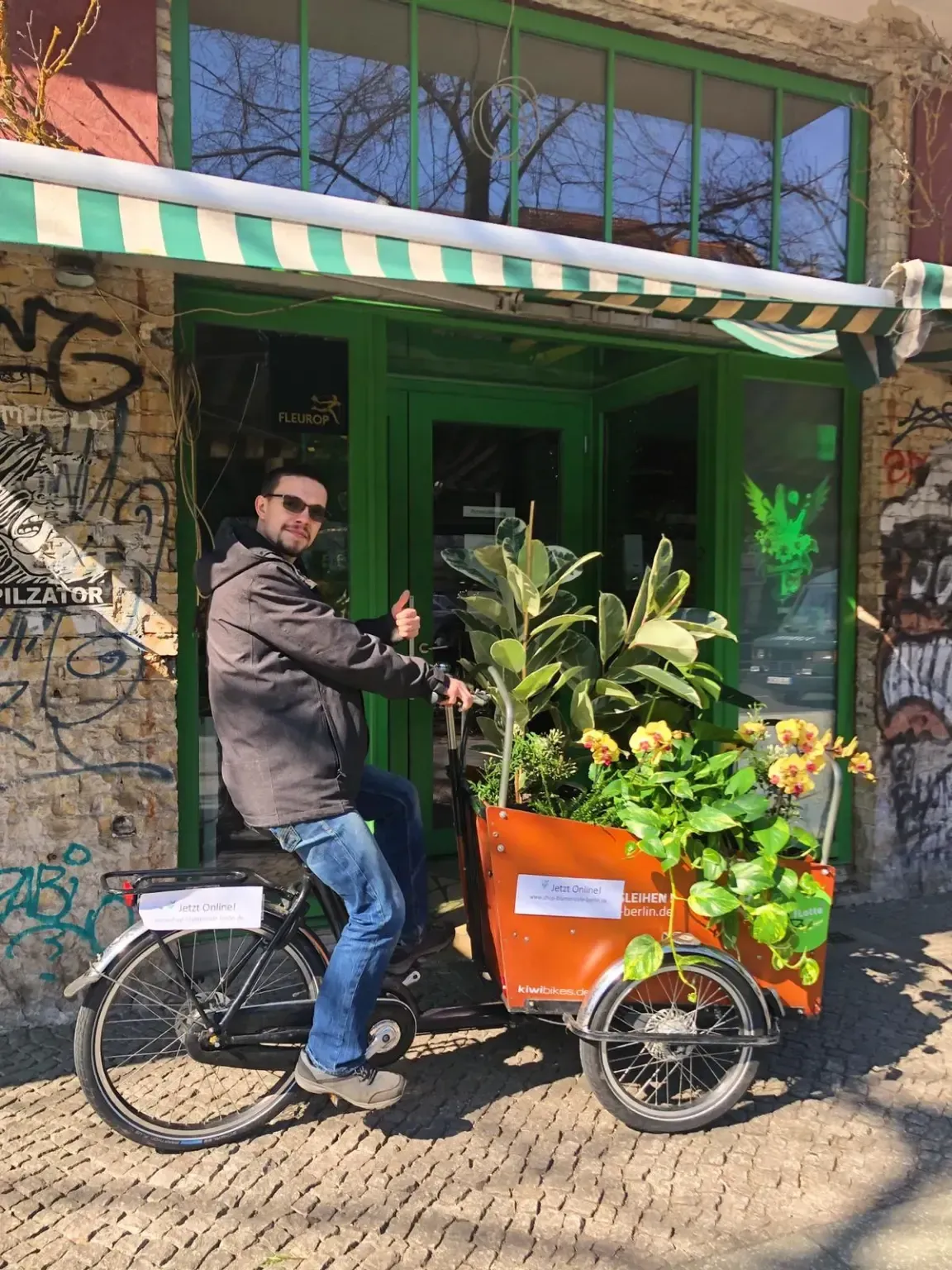 Ein Mann fährt mit einem Wagen voller Pflanzen auf einem Fahrrad.