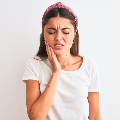 Mulher com expressão de dor, segurando o maxilar, provavelmente sentindo dor de dente.