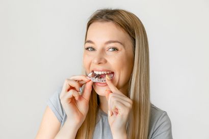 Mulher no dentista com a boca aberta, mãos enluvadas de azul segurando instrumentos odontológicos.