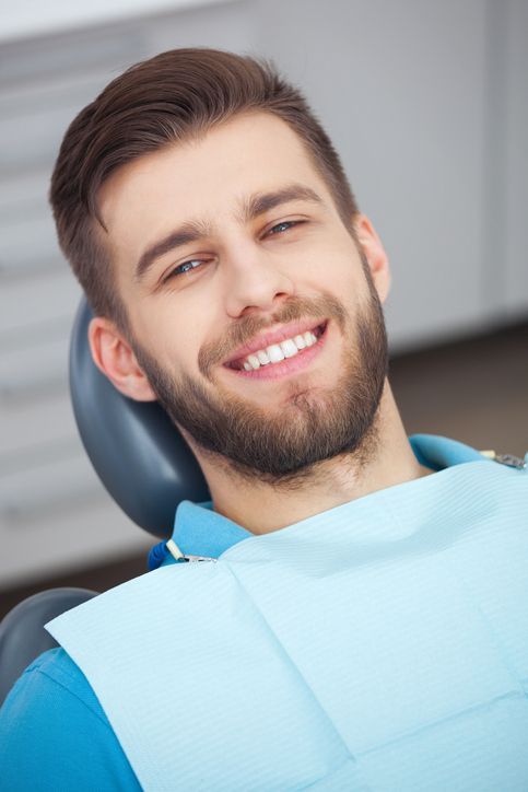 Homem com cabelos grisalhos faz careta, segurando a bochecha com dor, indicando dor de dente.
