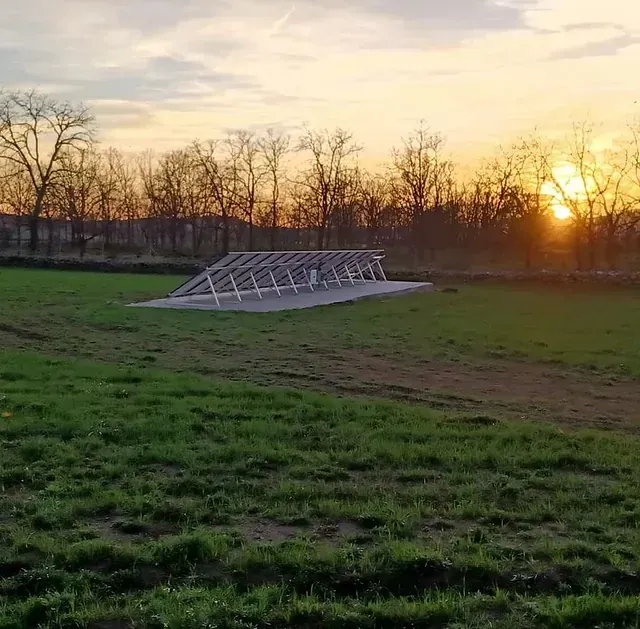 El sol se está poniendo sobre un campo de hierba con árboles al fondo.