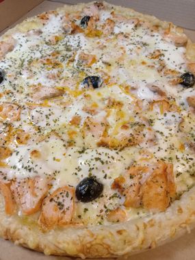 Pizza au fromage garnie de saumon, d'olives noires et d'herbes aromatiques sur une assiette