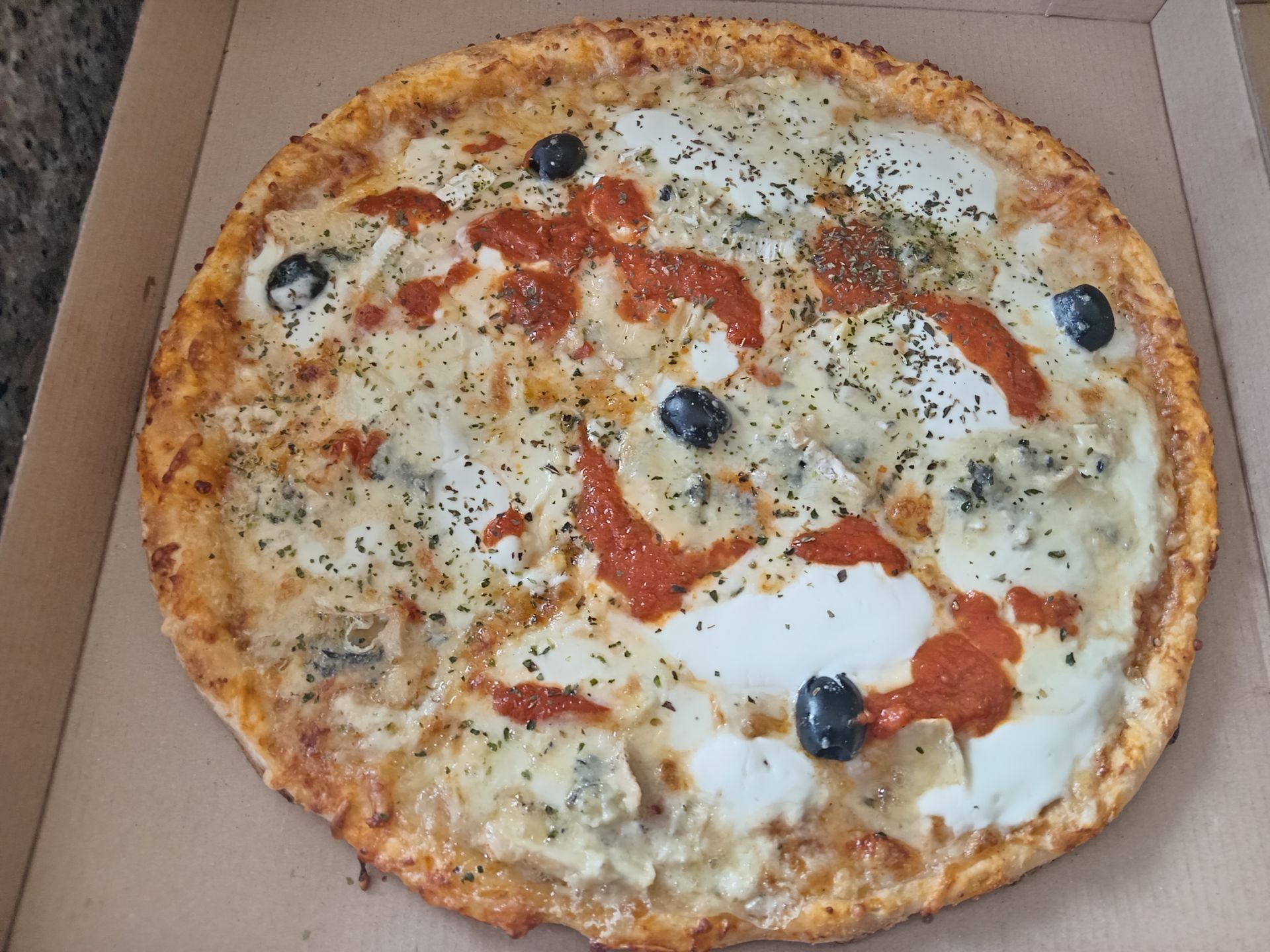 Pizza pepperoni aux olives noires dans une boîte en carton ouverte.