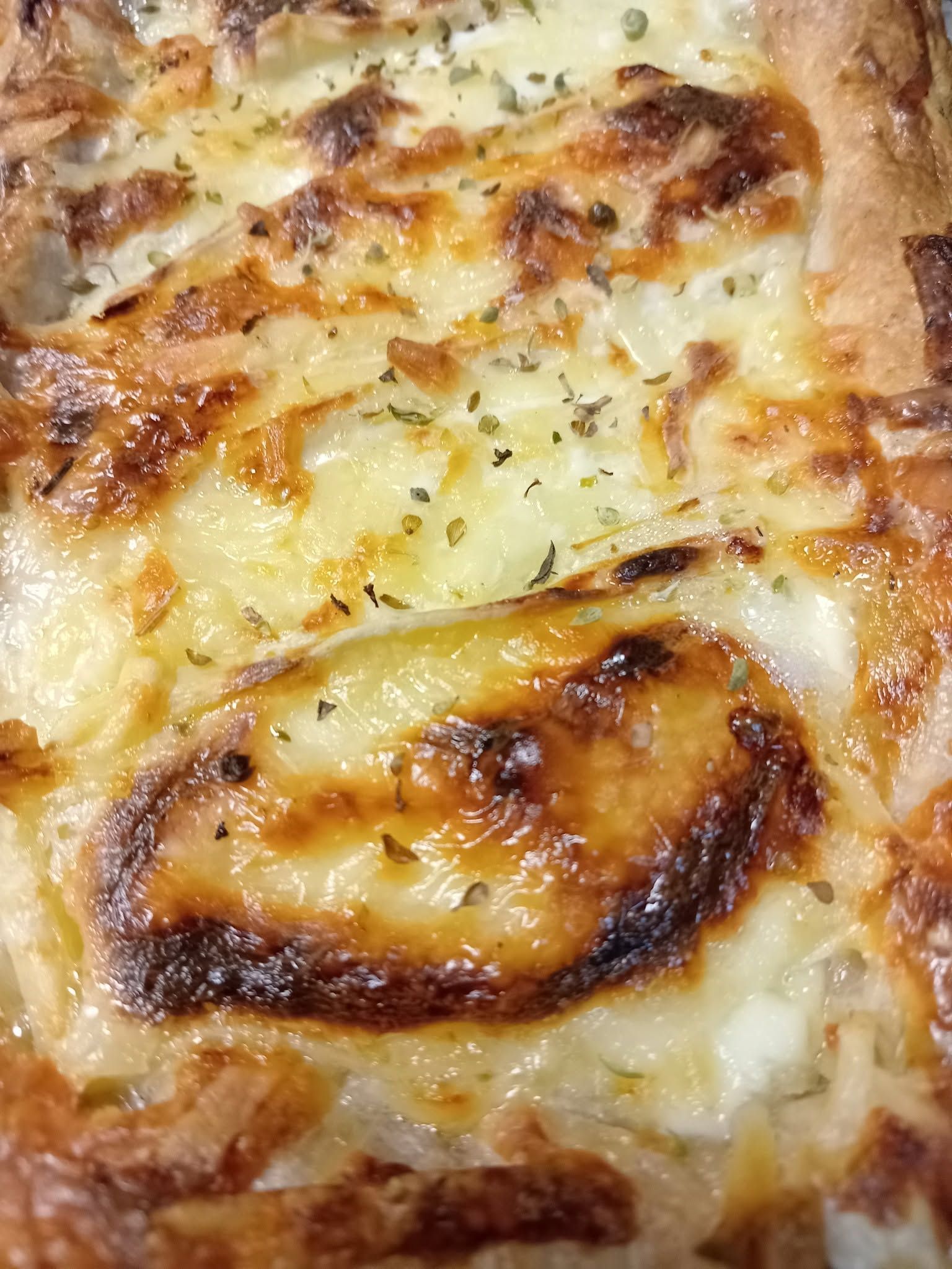 Tarte rustique aux noix et au fromage sur une table en bois avec des herbes et un bol de noix.