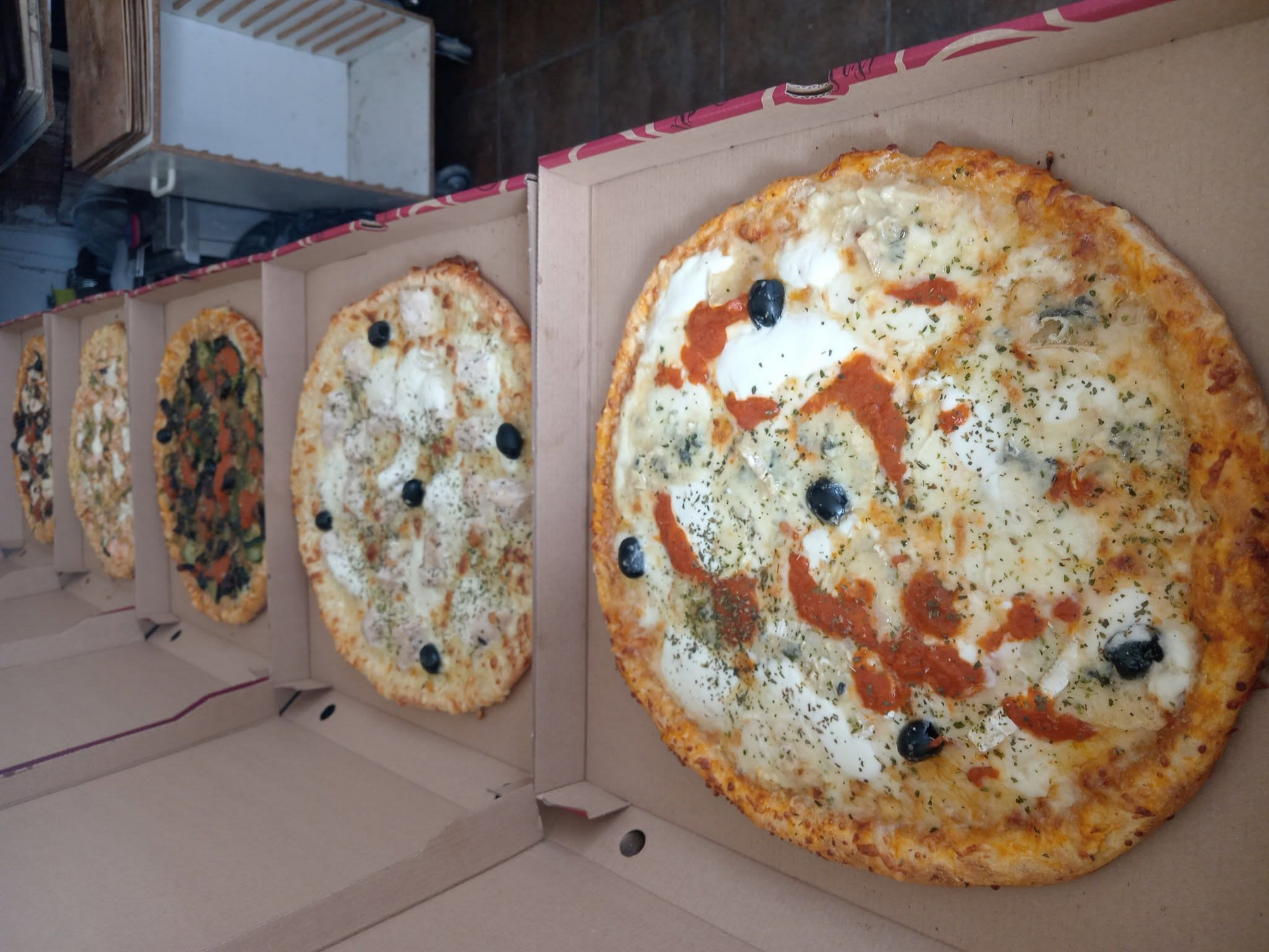 Plusieurs pizzas dans des boîtes ouvertes, avec notamment des garnitures au fromage, au pepperoni et aux légumes.