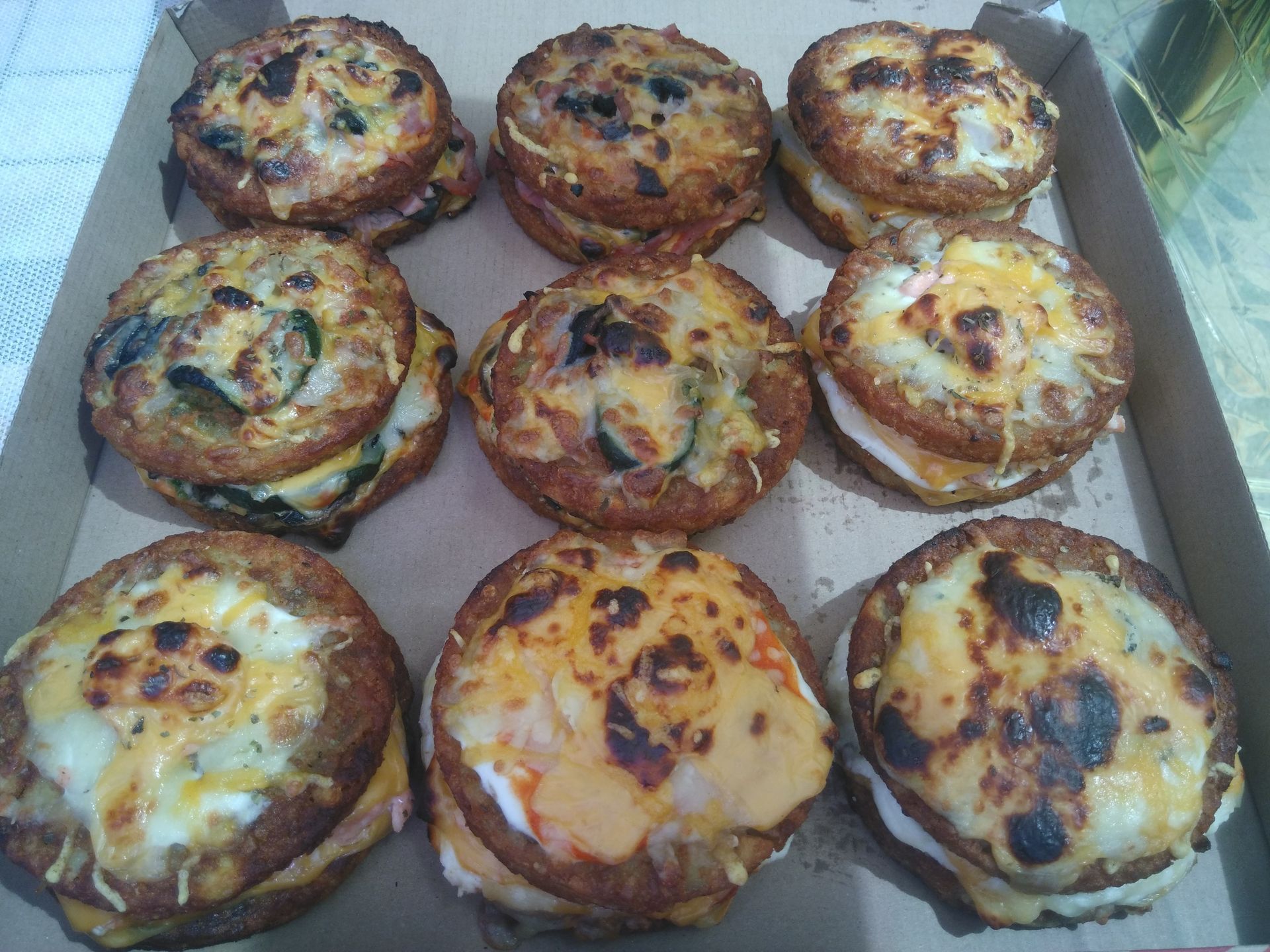 Neuf mini-pizzas cuites au four dans une boîte en carton, avec du fromage gratiné et des garnitures.