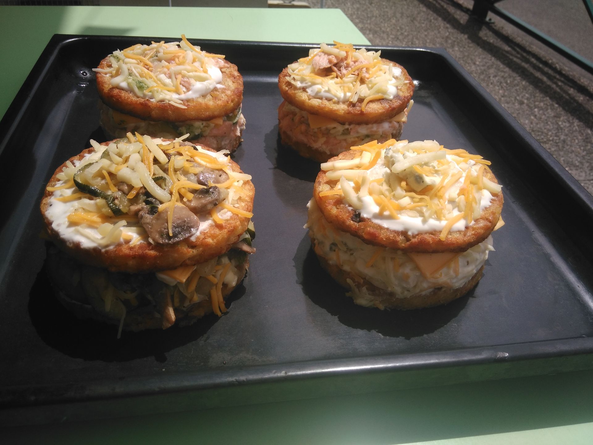Quatre mini-pizzas farcies, recouvertes de fromage râpé, sur une plaque de cuisson noire.