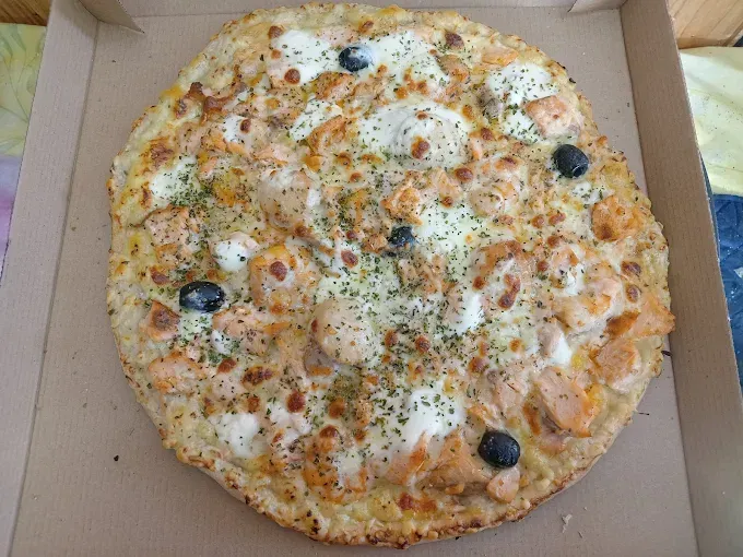 Pizza ronde au fromage, olives noires et herbes, dans une boîte en carton ouverte