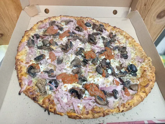 Une pizza aux olives, oignons, champignons et sauce tomate dans une boîte en carton