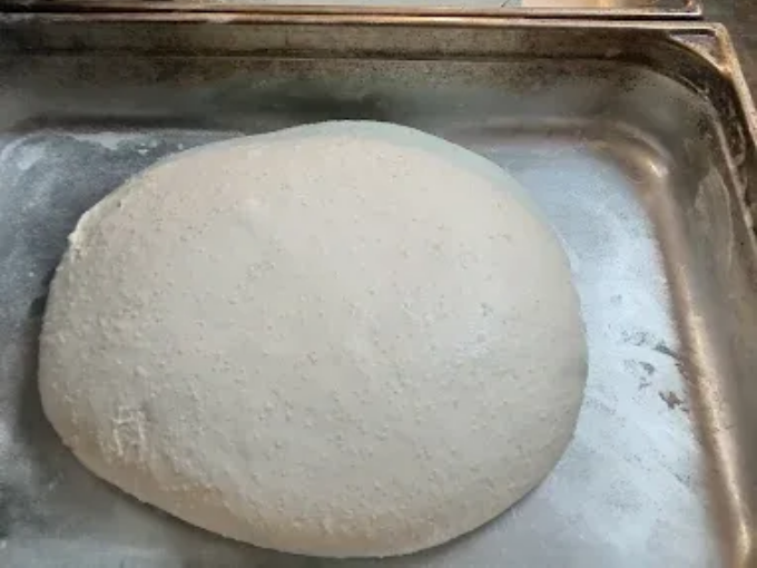 La pâte lève sur une plaque de cuisson en métal saupoudrée de farine.