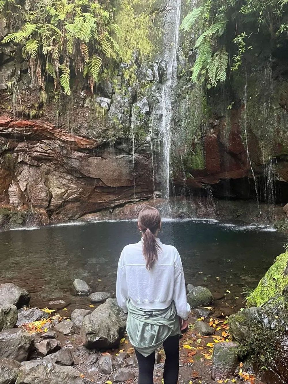 Eine Person steht vor einem Wasserfall in einem felsigen Waldbecken