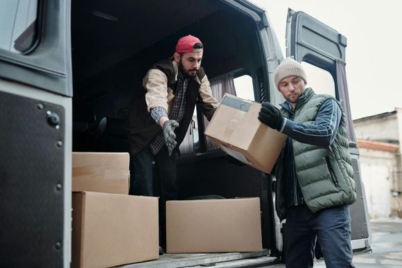 Dos personas cargan cajas de cartón en una camioneta desde un muelle de carga.