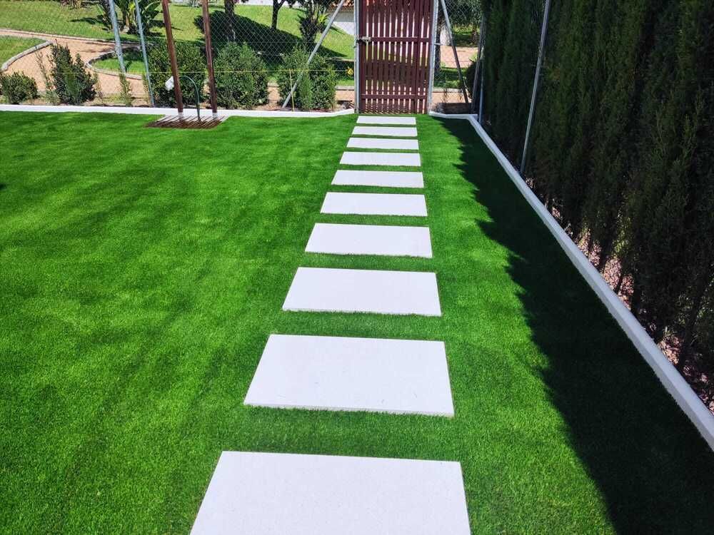 Unas losas blancas atraviesan un césped de un verde brillante y conducen a una puerta de madera.
