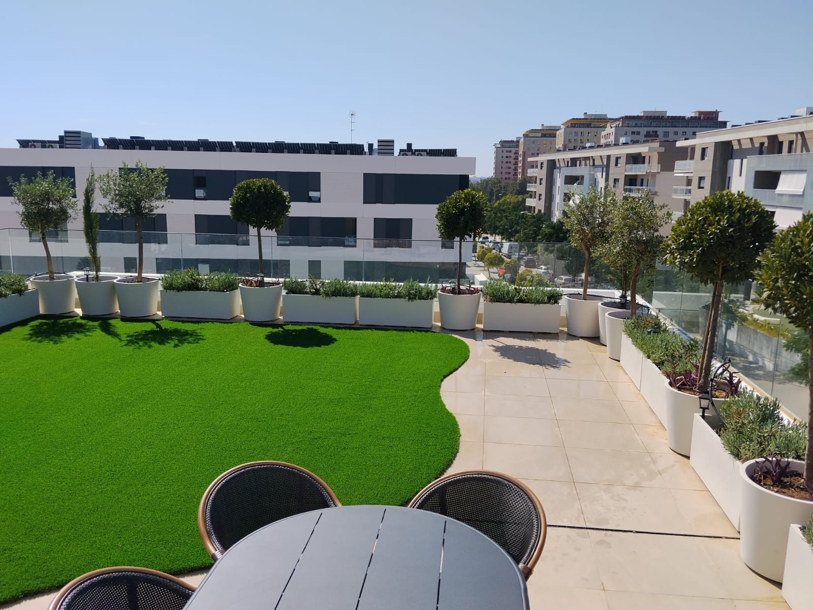 Terraza en la azotea con césped, sillas de patio y edificios de la ciudad al fondo.