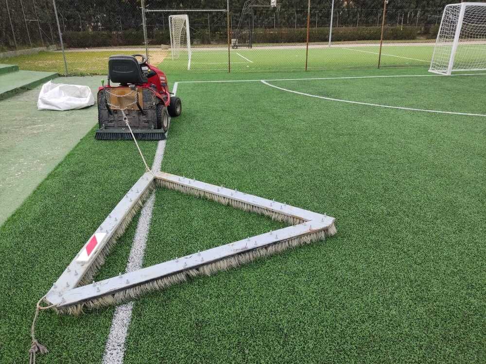 Marcador triangular blanco de un campo de fútbol sobre césped verde junto a un carrito y porterías a lo lejos.