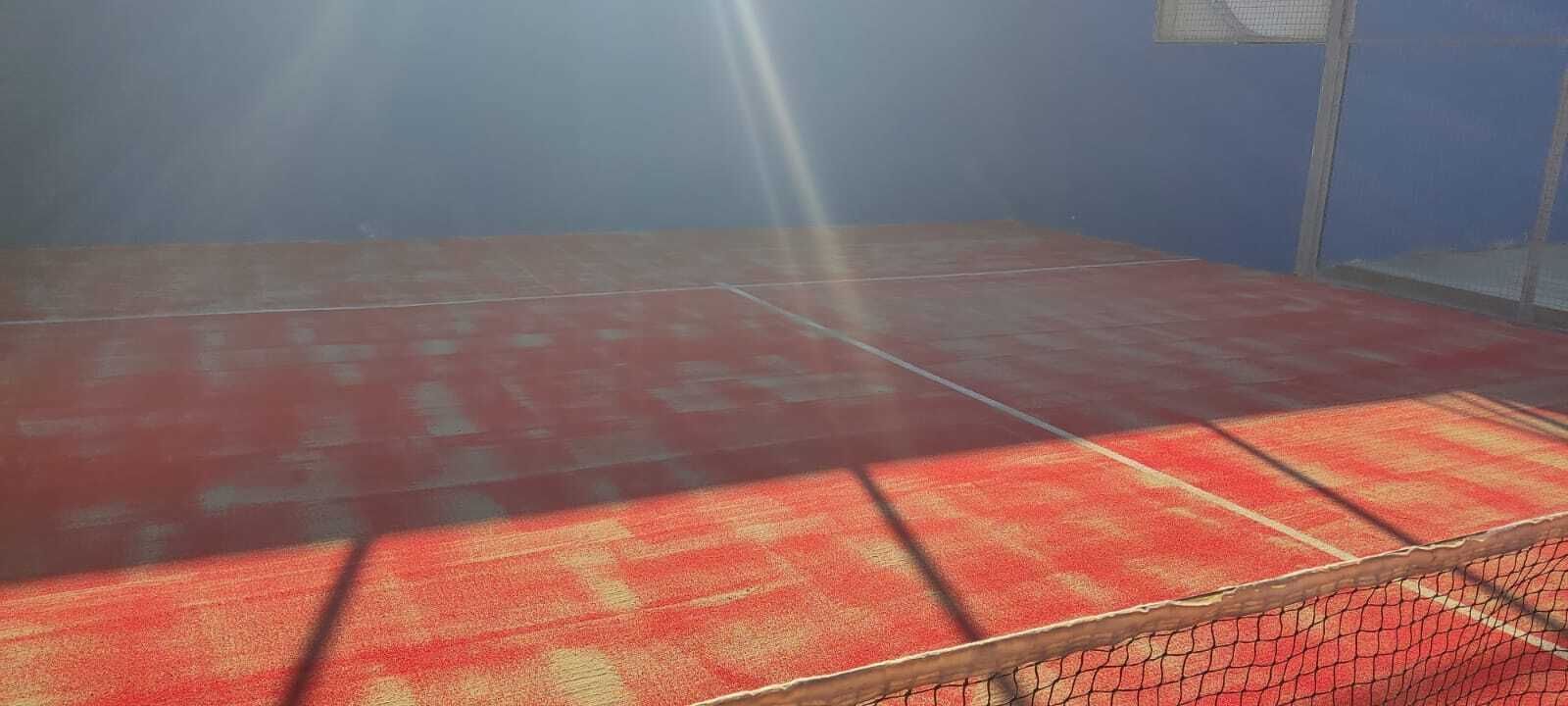 Suelo alfombrado de color rojo iluminado por el sol en una habitación interior brumosa, con una pared baja y un fondo sombreado.