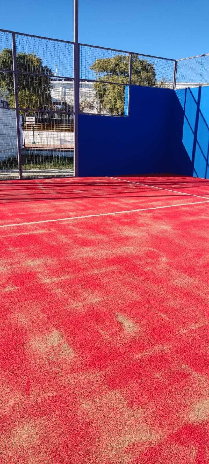 Pista deportiva roja al aire libre con paredes azules y valla negra bajo un cielo despejado.