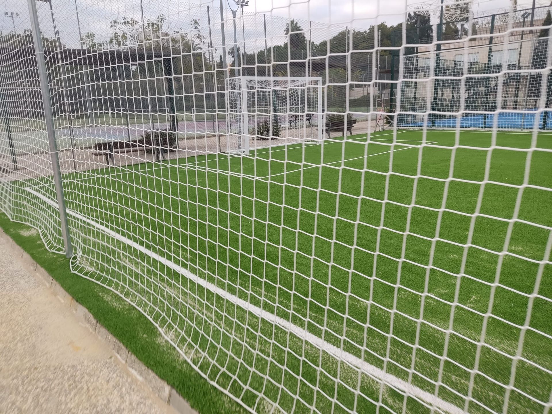 Red de portería de fútbol junto a un campo verde con una pista de atletismo y edificios al fondo.