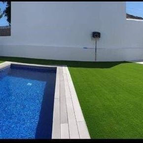 Una piscina rodeada de césped artificial en un patio trasero.