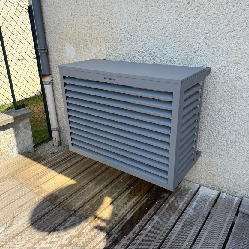 Un meuble d'extérieur gris à persiennes, adossé à un mur sur une terrasse en bois, projette une ombre.