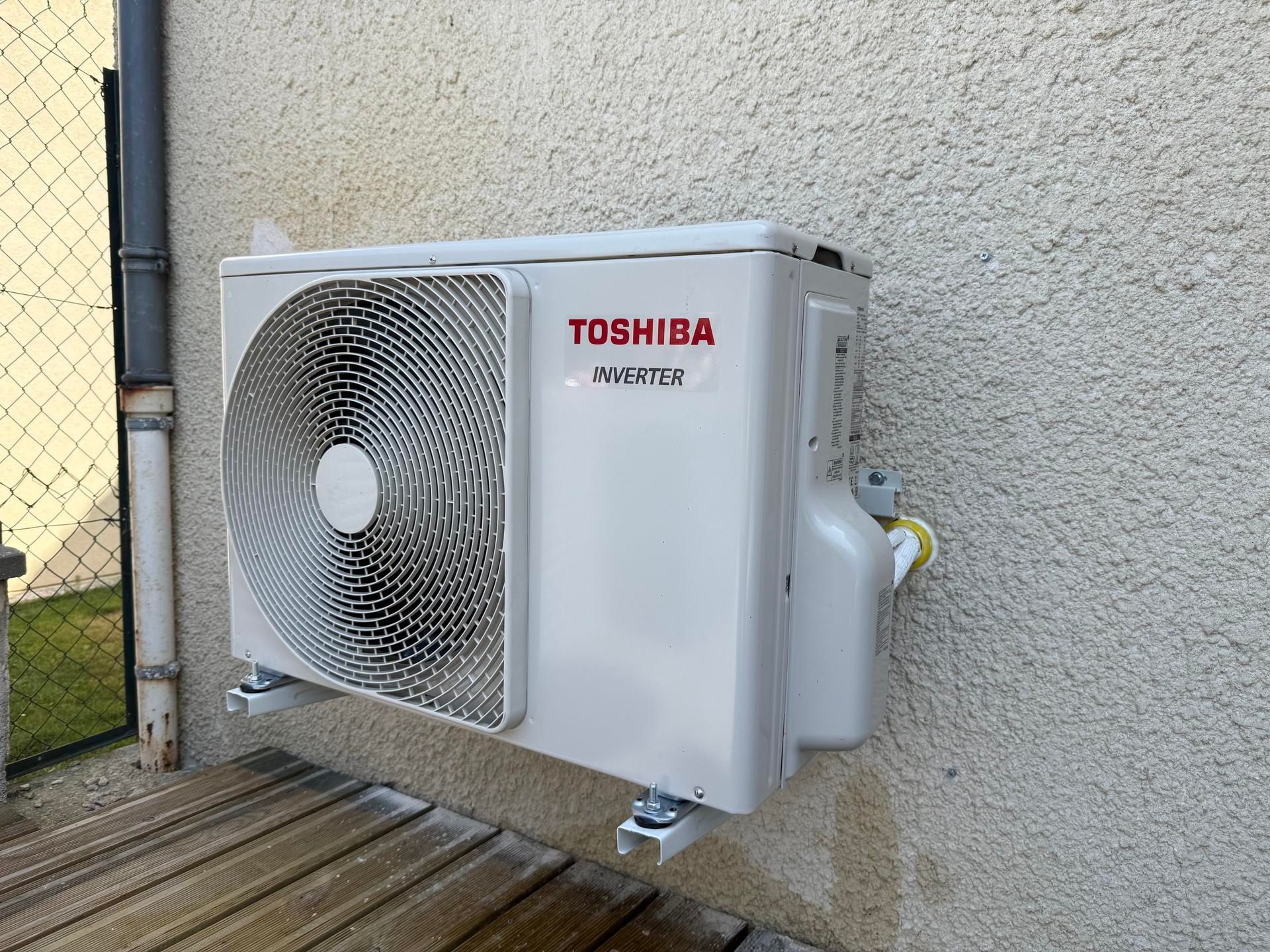 Unité de climatisation extérieure Toshiba montée contre un mur sur une terrasse en bois.