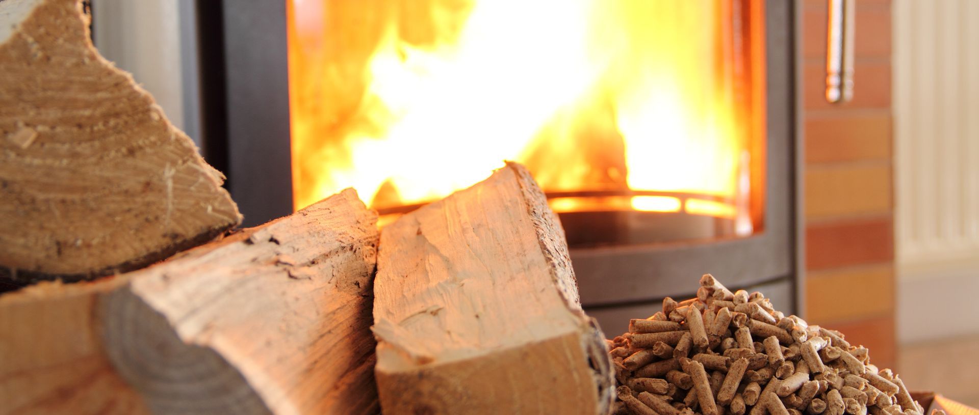 Bois de chauffage empilé à côté d'une cheminée incandescente dont les flammes sont visibles en arrière-plan.