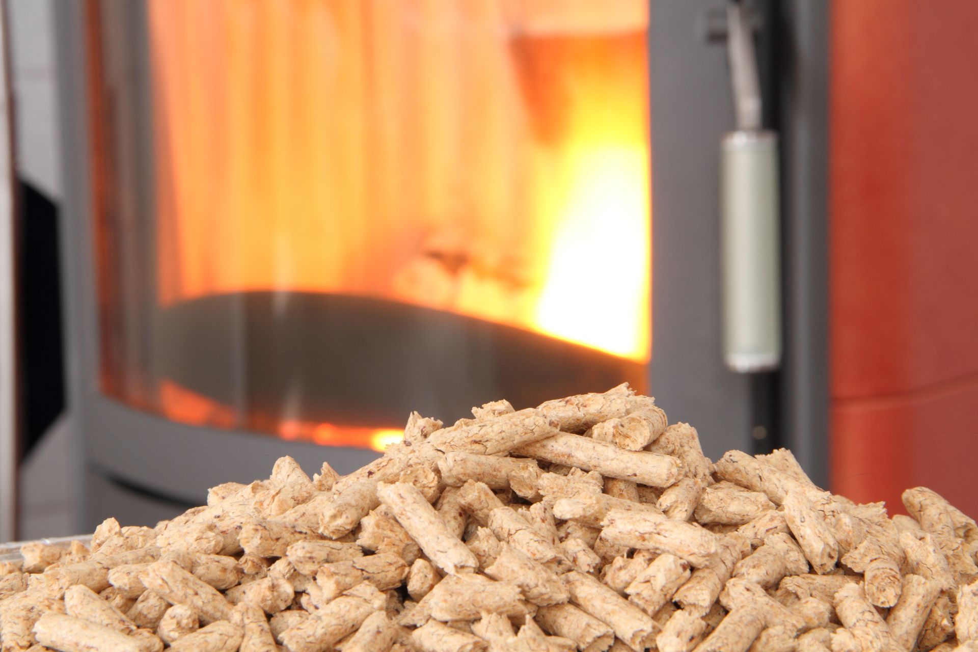 Des granulés de bois empilés devant un poêle à granulés incandescent dont les flammes sont visibles.