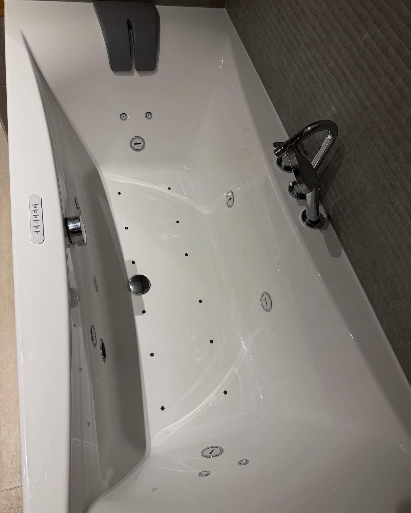Baignoire blanche avec robinetterie chromée et douchette à main sur un mur de salle de bains carrelé foncé.