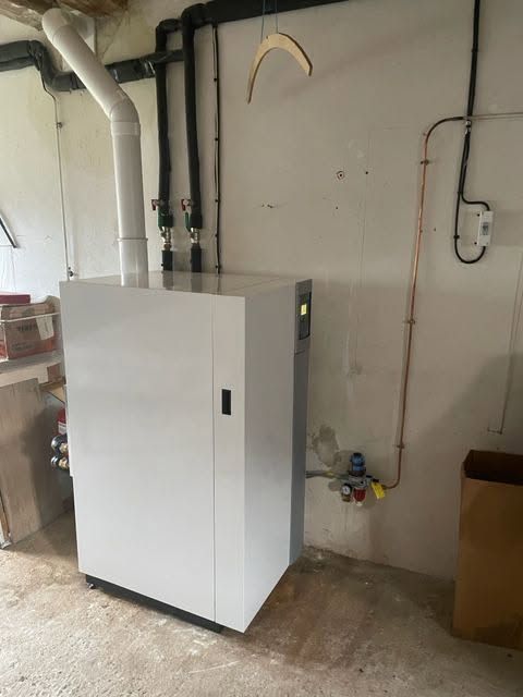 Armoire blanche ou chaudière dans une buanderie au sous-sol, avec tuyauterie et murs apparents.