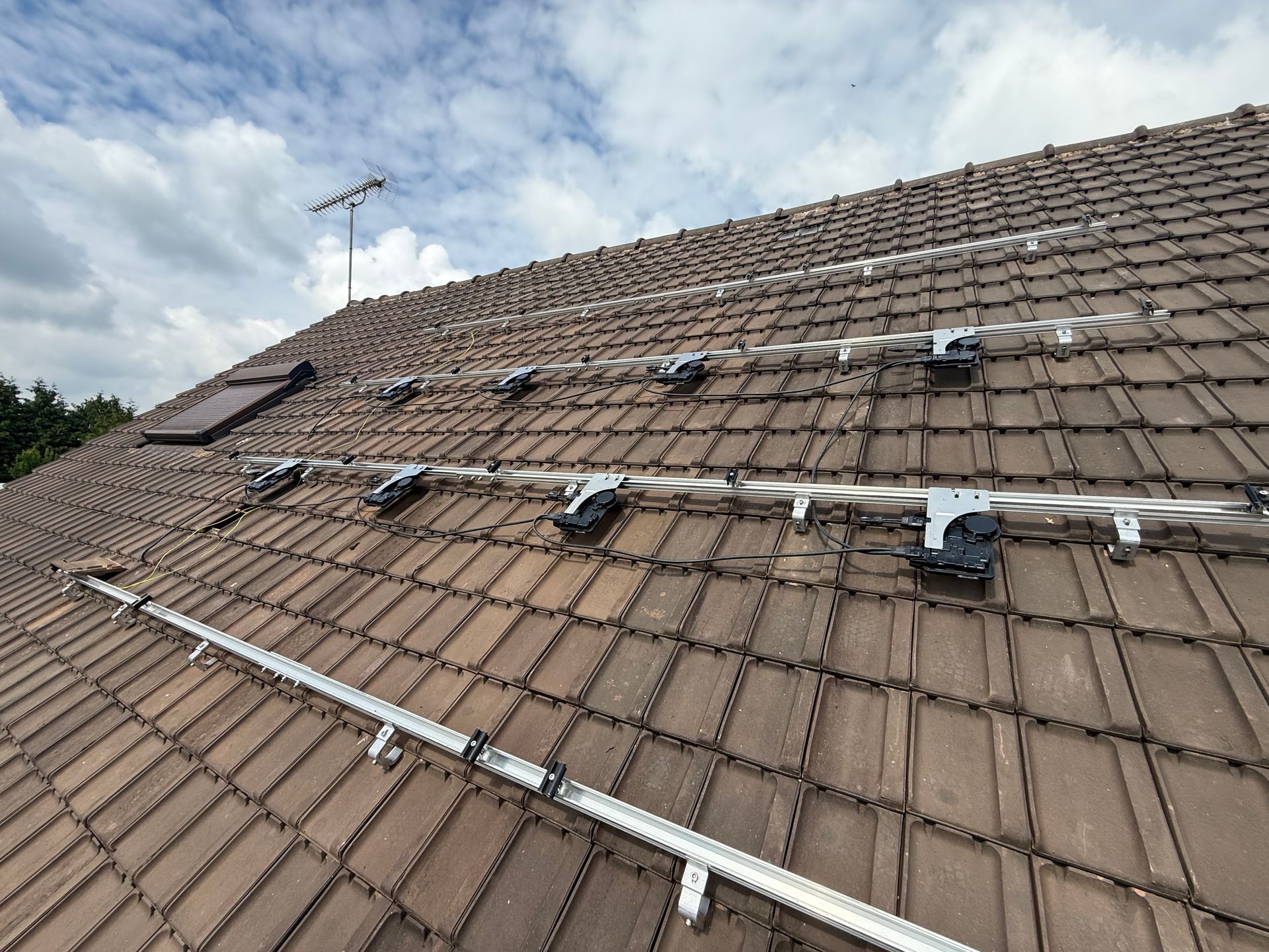 Matériel de montage pour panneaux solaires sur un toit de tuiles sous un ciel nuageux.